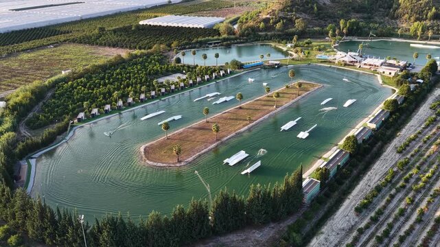 World class wakepark in Antalya, Turkey, with riders on crystal clear lakes surrounded by palm trees and mountains and multiple water obstacles for wakeboarding. Cable Wake park in Turkey.