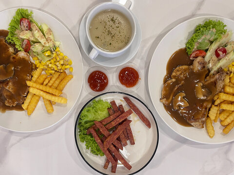 Colorful restaurant meal featuring fries, grilled meat, vegetables, sauce and soup, presented as a varied casual dining spread.