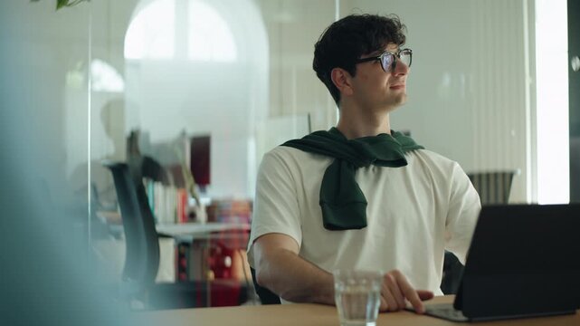 Thoughtful man sits at a desk with a tablet during a business meeting, conveying communication, concentration, and professional presence in an indoor office environment.