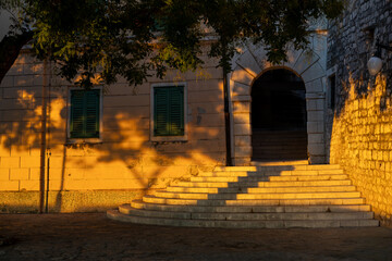 Historic stone entrance and steps in  old town glowing in low evening sunlight, suitable for Croatian travel, heritage architecture and Mediterranean lifestyle themes © Evgeniia