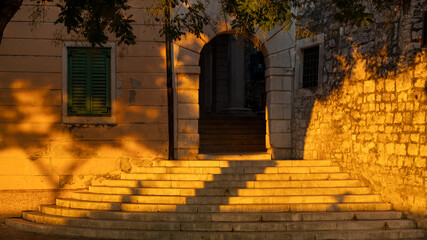 Wide stone staircase leading through a historic archway in Croatia, illuminated by golden evening light for travel, architecture and cultural heritage themes © Evgeniia