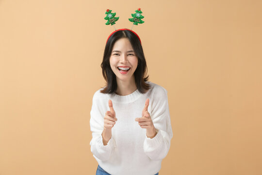 Cheerful Asian woman wearing a white sweater and giving two thumbs up, Christmas celebration, festive holiday spirit concept.