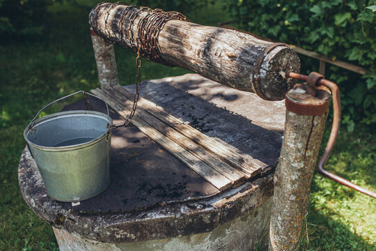 Old rustic wooden water well with metal bucket in rural garden. Nostalgia, rural simplicity, traditional living. Historical methods of water extraction, sustainable country life, aesthetic beauty.