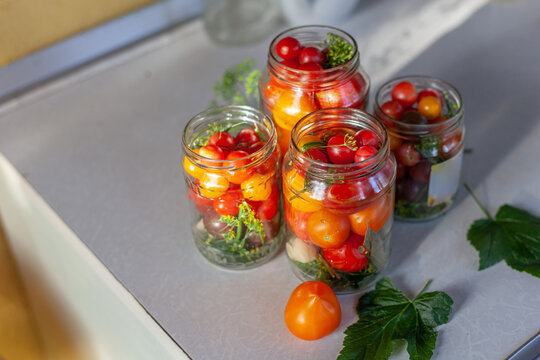 Glass jars filled with fresh cherry tomatoes, herbs, spices, prepared for pickling and canning. Process of preserving fresh vegetables at home. Organic healthy food, seasonal food preparation.