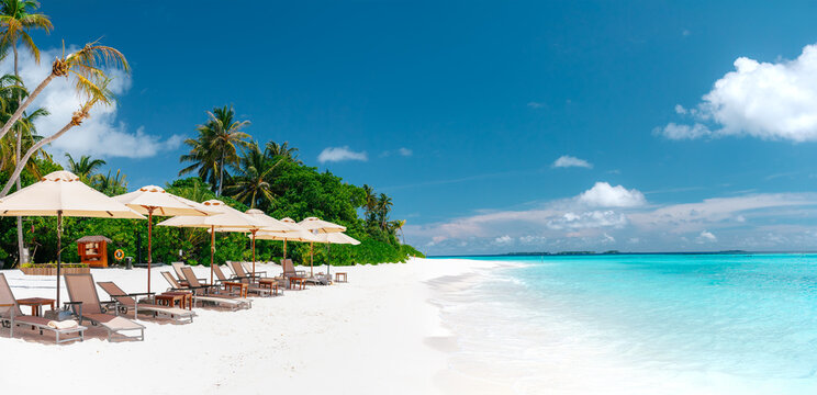 Tropical luxury beach resort with white sand, beach umbrellas, sun loungers, palm trees and turquoise ocean water