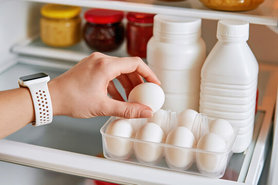 Hand taking egg from a plastic carton in refrigerator, focusing on healthy eating and food storage