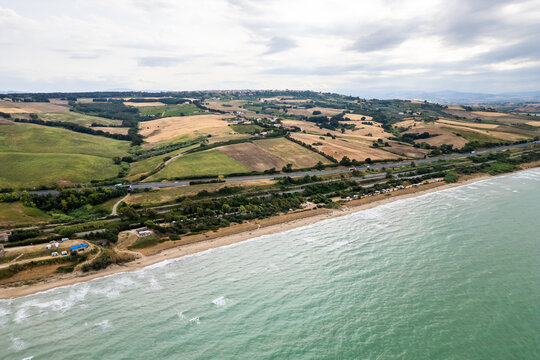 Aerial view of the Molise coast in Italy, showing a sandy beach along the turquoise Adriatic Sea. A coastal road, railway, highway, and seaside campsite border rolling agricultural fields and
