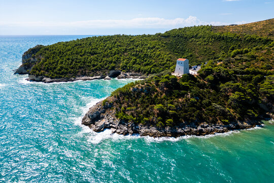 A vibrant aerial view of Torre di San Felice perching on the dramatic cliffs of Gargano in Puglia, Italy. The ancient watchtower stands above turquoise Adriatic waters, surrounded by green hills