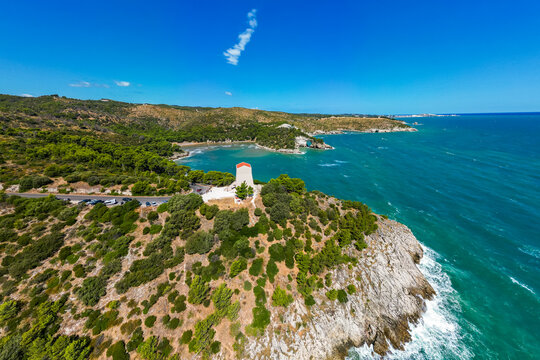 A vibrant aerial view of Torre di San Felice perching on the dramatic cliffs of Gargano in Puglia, Italy. The ancient watchtower stands above turquoise Adriatic waters, surrounded by green hills