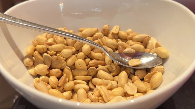 VIdeo of roasted skinless peanuts fill a white ceramic bowl with a metal spoon resting on top