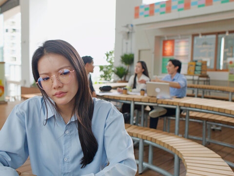 Thoughtful Asian Businesswoman Sitting Separately From Colleagues in Modern Office