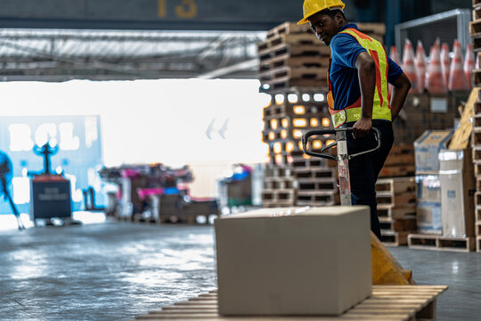 A warehouse worker turns the pallet truck towards the shipping area in front of the open shutter of the loading bay during a routine inventory check as part of the daily supply chain
