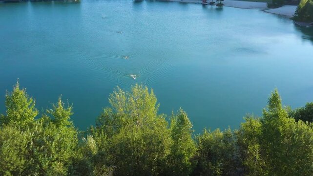 The lake is located in an abandoned quarry with blue water. Scenic aerial view of an abandoned quarry with clear blue water transformed into a public beach and recreational park with swimmers.