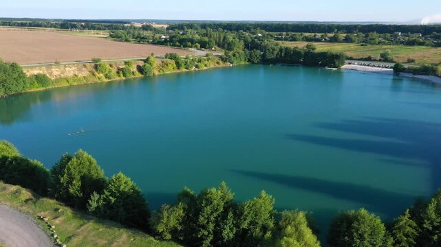 The lake is located in an abandoned quarry with blue water. Scenic aerial view of an abandoned quarry with clear blue water transformed into a public beach and recreational park with swimmers.