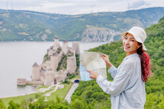 Smiling female tourist holds a map overlooking the historic Golubac fortress and Danube river below in Serbia