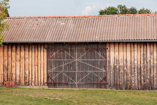 Symmetrically framed weathered wooden barn with large slatted double doors and corrugated metal roof in a rural setting. Agriculture concept.