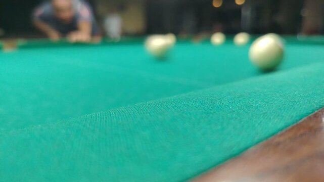 Player hitting billiard balls on a green table during a game. Close-up of billiard balls rolling on a green table during a game indoors