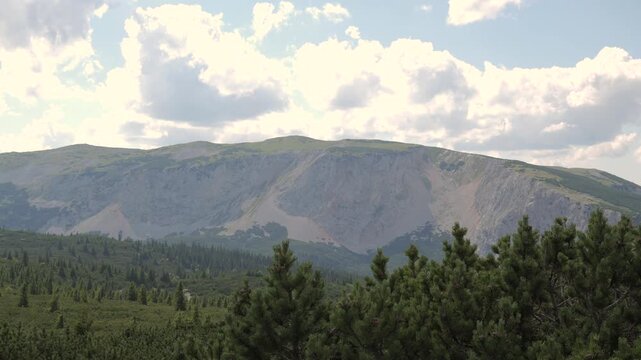 Mountains rise with greenery below while clouds move across the sky over time.