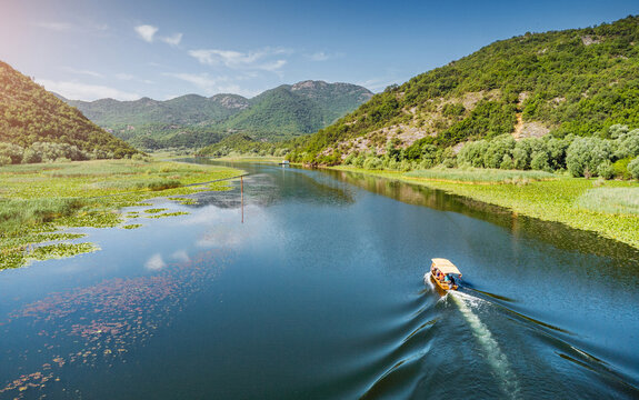 Motorboat making waves, sailing past lush green mountains and vast fields of water lilies on a sunny day in Skadar, Montenegro