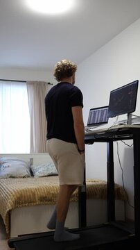 Vertical screen frustrated remote worker is fed up with his daily routine and stares at the monitor while walking on a treadmill feeling bored with repetitive computer work