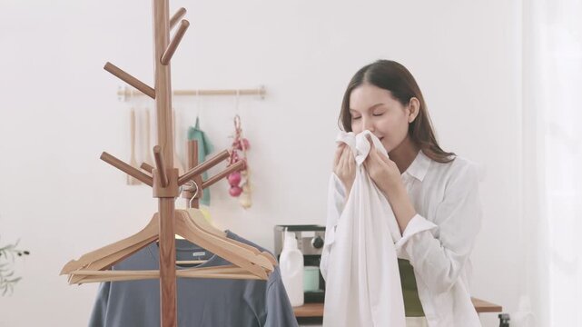 A smiling Asian woman doing laundry at home. She hangs a t-shirt on a wooden clothes rack.