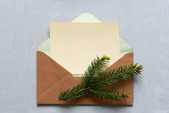 Elegant Christmas greeting card with blank cream paper, kraft envelope and fresh evergreen pine branch on soft gray background, festive winter holiday stationery and copy space design