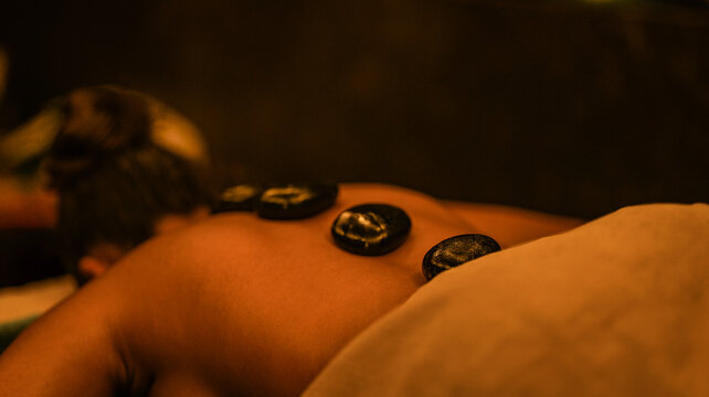 A woman receiving a relaxing hot stone massage treatment in a dimly lit professional spa setting