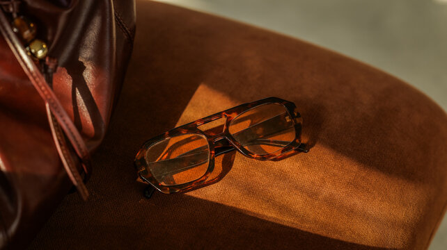 Tortoiseshell sunglasses resting on a soft brown velvet surface with a leather handbag nearby