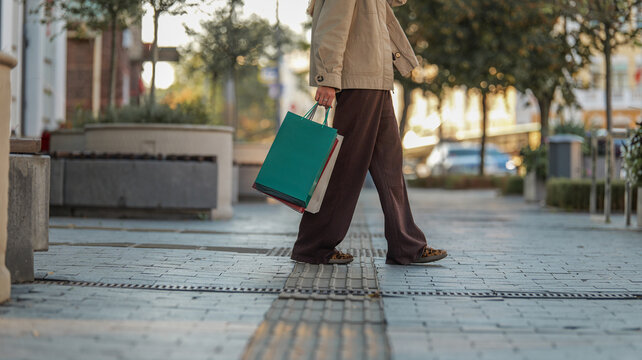 Person walking on a paved city sidewalk carrying colorful shopping bags during the daytime