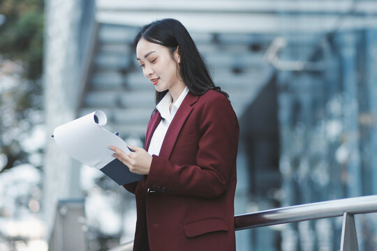 Young professional woman talking on phone and holding coffee outside modern office building