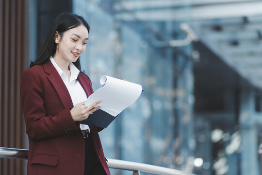 Young professional woman talking on phone and holding coffee outside modern office building