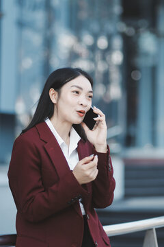 Young professional woman talking on phone and holding coffee outside modern office building