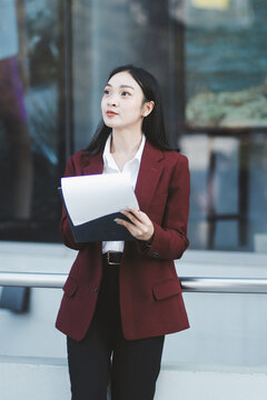 Young professional woman talking on phone and holding coffee outside modern office building