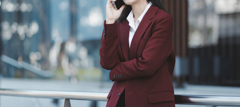 Young professional woman talking on phone and holding coffee outside modern office building