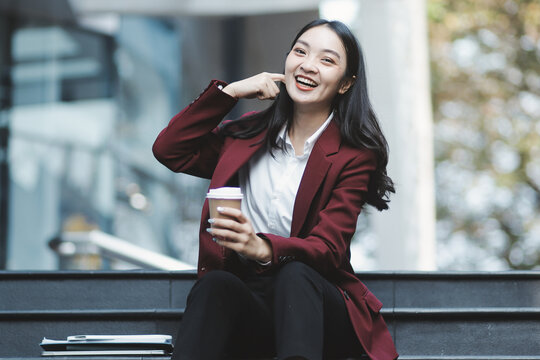 Focused woman in blazer types on laptop outdoors. Urban professional works remotely on stairs. She uses modern tech for business and connection.