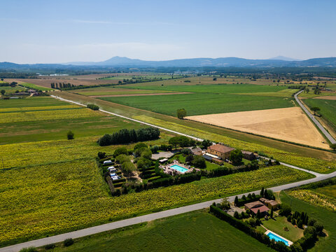 An aerial drone view reveals a charming Tuscan agriturismo nestled among vibrant sunflower fields and vast farmland. The property features a swimming pool and an organized camperstop for motorhomes in