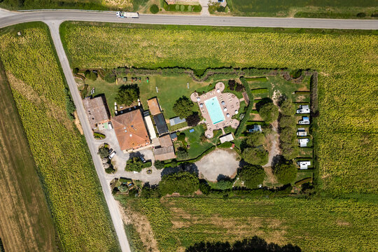 An aerial drone view reveals a charming Tuscan agriturismo nestled among vibrant sunflower fields and vast farmland. The property features a swimming pool and an organized camperstop for motorhomes in