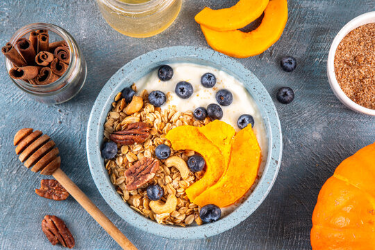 Healthy autumn breakfast bowl with yogurt, granola, nuts, baked pumpkin and blueberry