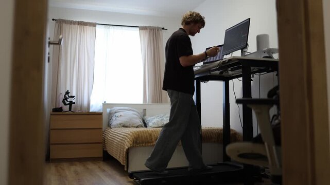 Frustrated young trader struggles to learn financial market basics while walking on a treadmill reacting with confusion to complex stock charts during his online study session