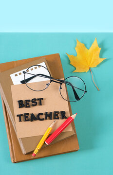 Teacher's day holiday, education concept. Greeting card "best teacher" of wooden letters, pencils, books, eyeglass, yellow maple leaf on table close up. top view