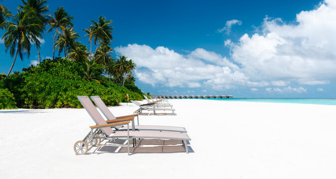 Tropical luxury beach resort with white sand, beach umbrellas, sun loungers, palm trees and turquoise ocean water
