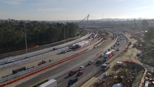 Aerial drone footage of EastLink freeway works in Doncaster, Melbourne at sunset, showing major interchange construction, elevated road structures, traffic and large-scale infrastructure upgrades.