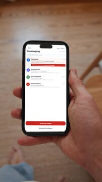 An email inbox shows a warning banner above a message from a suspicious sender. Point of view shot in vertical format with the phone held in the hand. Interface in German.