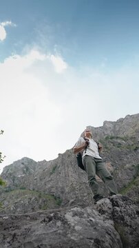 Young female hiker with a backpack standing on a rock and enjoying a breathtaking mountain view, capturing hiking, adventure, freedom and exploration in nature.