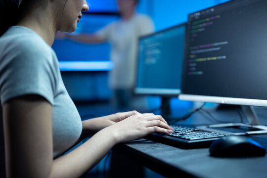 Close up of young female software engineer writing program code on multiple desktop screens in a modern office.