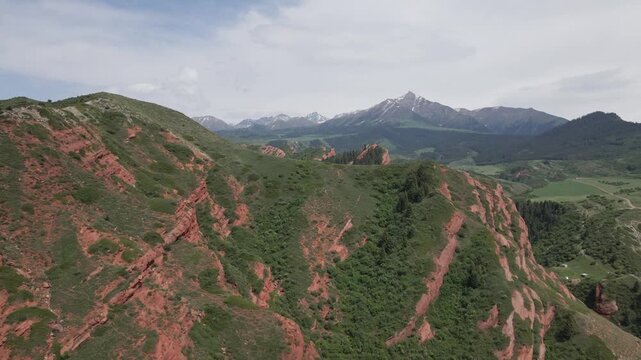 Aerial drone view of the red and green mountains of Jeti Oguz Gorge with distant snow-capped peaks in Kyrgyzstan