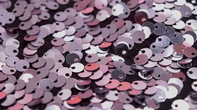 Close-up rotating shot of shimmering silver and red sequins on black fabric background, highlighting texture and light reflection