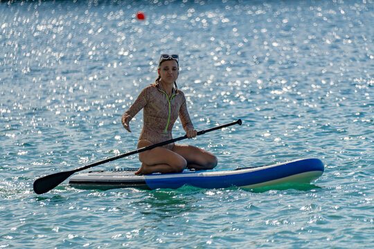 Paddleboarding, woman, water. Woman kneeling on a stand up paddleboard in glittering blue sea enjoying watersports.