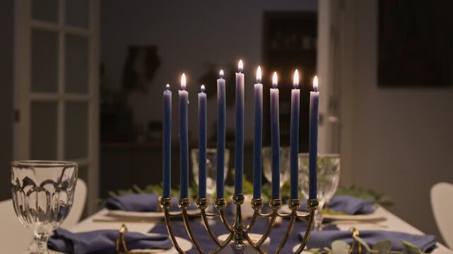 Traditional Hanukkah menorah with burning blue candles standing on decorated holiday table. Footage serves Jewish culture campaigns, holiday marketing, and seasonal advertising