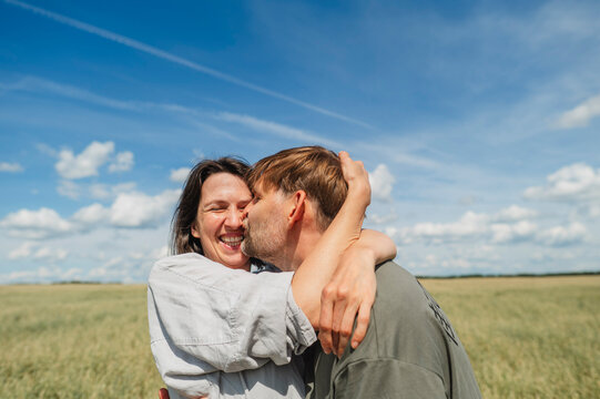 Man kisses smiling woman while embracing in a sunny field